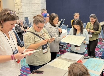 Several people standing around a table looking down at a white thin board they're holding.